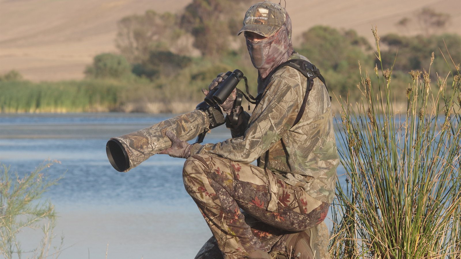 Photographer with a long telephoto lens crouching beside still water